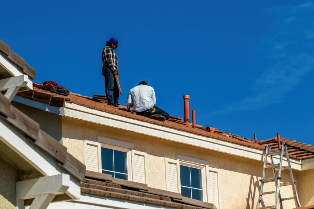 Deux couvreurs installant des tuiles sur un toit en pente avec ciel bleu